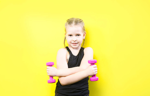 Theme sport and health. Beautiful caucasian child girl with pigtails posing on yellow background with smile. little athlete holding pink dumbbells. Banner for advertising, space for text copy space - Fotografie, Obrázek