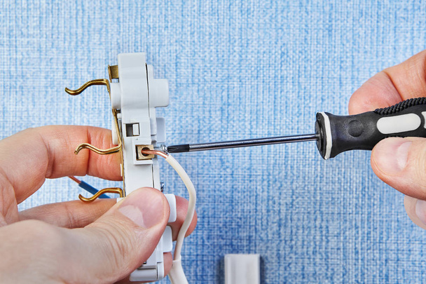 Worker tightens screw in wall plug. - Zdjęcie, obraz