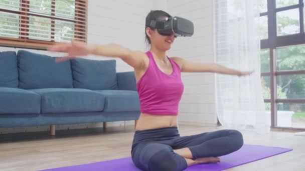 Young Asian teenager woman using virtual reality simulator while practicing yoga in living room, female working out for healthy at home. Lifestyle woman exercise future technology concept concept. - Metraje, vídeo