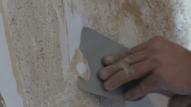 Homme nettoie les murs d'argile de vieux papier peint avec une spatule vue de près
 - Séquence, vidéo