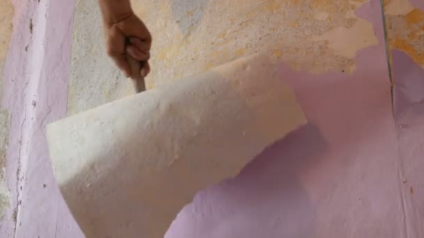 A férfi építők letépi vagy héj régi rózsaszín tapéta a falról, egy különleges spatula - Felvétel, videó