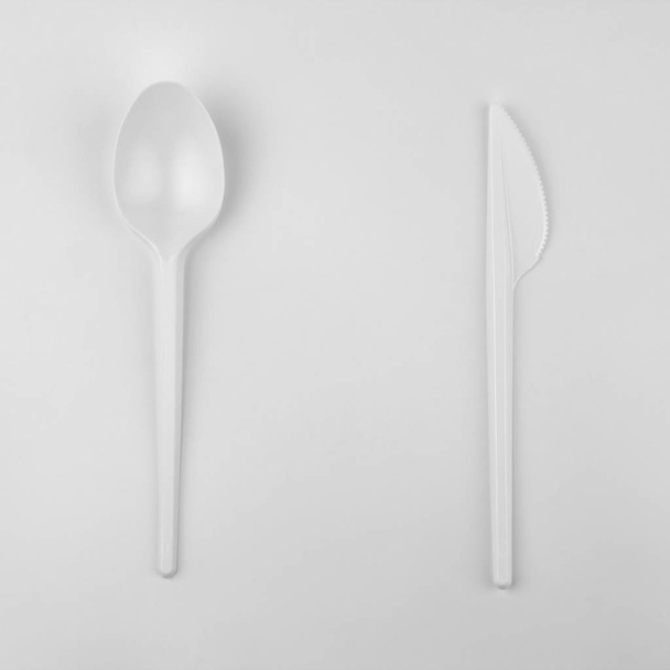 clear white plastic spoon and knife on white background, ecological problem, closeup, square photo - Fotó, kép