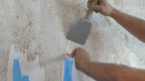 Mann reinigt die Lehmwände von alten Tapeten mit einem Spachtel aus nächster Nähe - Filmmaterial, Video