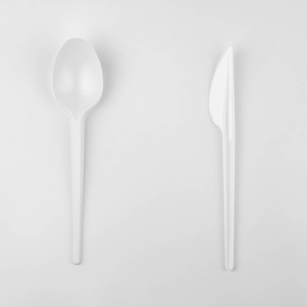 clear white plastic spoon and back side of knife on white background, ecological problem, closeup, square photo - Photo, Image