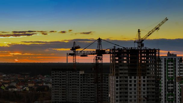 Вечерняя строительная площадка с высоким краном на фоне солнечного заката с красным небом
 - Фото, изображение