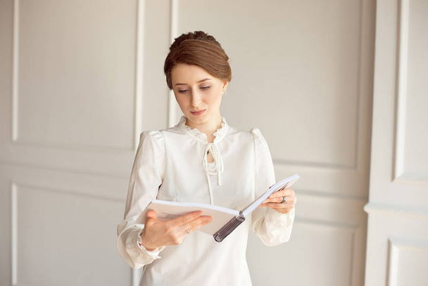 Business woman in a white shirt and black trousers looks documents in hands. - Foto, afbeelding