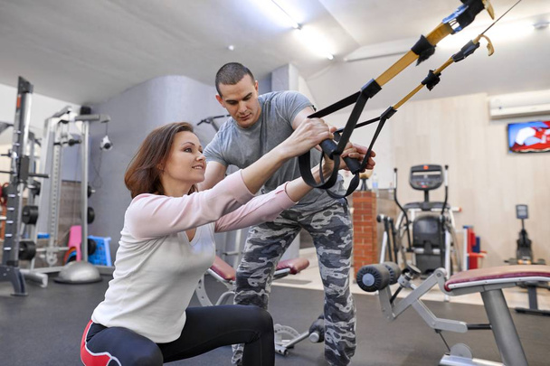 Mature woman exercising in gym using fitness straps loops. Male instructor assisting middle-aged woman - Fotoğraf, Görsel
