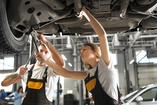 Professional mechanics standing under automobile and working - Zdjęcie, obraz