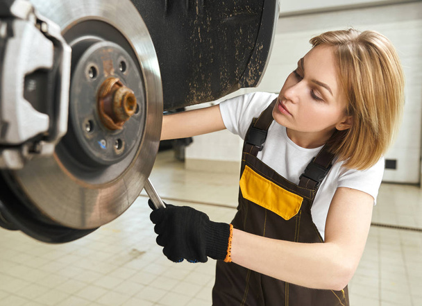 Keskittynyt nainen mekaanikko vaihtaa rengas auto työpaja
 - Valokuva, kuva