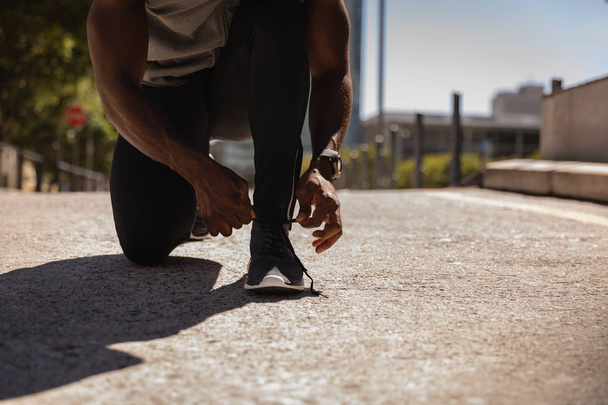 Puolivälissä mies sitominen hänen kenkä pitsi kun kyyristely jalkakäytävällä aurinkoisena päivänä
 - Valokuva, kuva