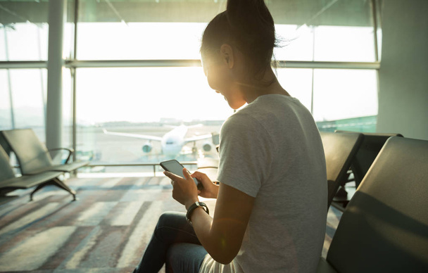 Γυναίκα επιβάτης που χρησιμοποιεί το κινητό τηλέφωνο στο αεροδρόμιο - Φωτογραφία, εικόνα