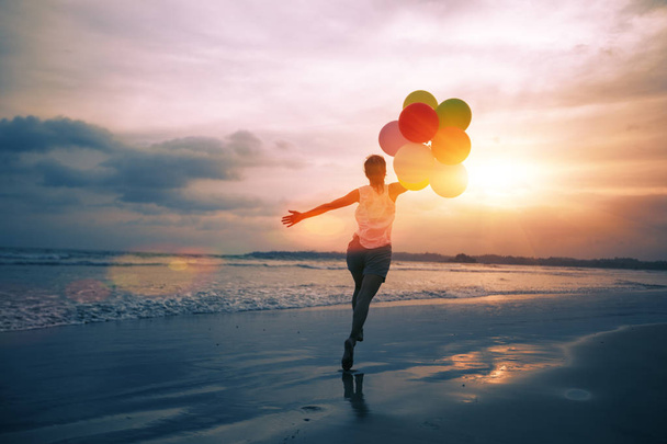 young woman running and jumping on seaside with colored balloons - Photo, Image