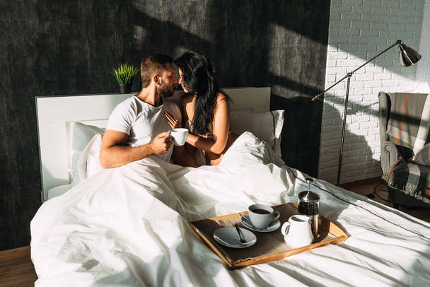 Beautiful couple in bed. Lovers in bed. Happy loving couple having breakfast in bed. Family relationships. Young couple drinking tea. Man and woman having Breakfast in their bedroom - Fotó, kép