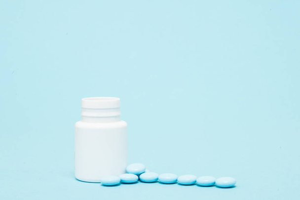 Blue pills and pill bottle on blue background - Фото, изображение