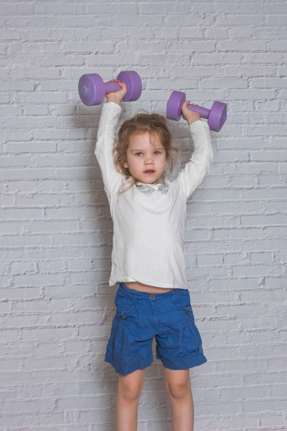 girl, the child is engaged in fitness with dumbbells, against a  - Zdjęcie, obraz