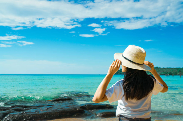 Jovem mulher asiática feliz em estilo casual moda com chapéu de palha stand na praia do mar de resort em férias de verão. Relaxar e desfrutar de férias na praia paradisíaca tropical. Vibrações de verão. Viagem de verão
. - Foto, Imagem