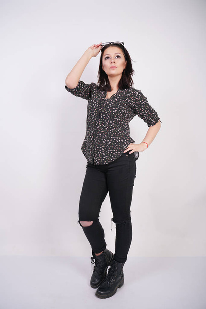 pretty teen girl wearing fashion casual shirt and black torn jeans posing with eyeglasses on white studio background - Φωτογραφία, εικόνα