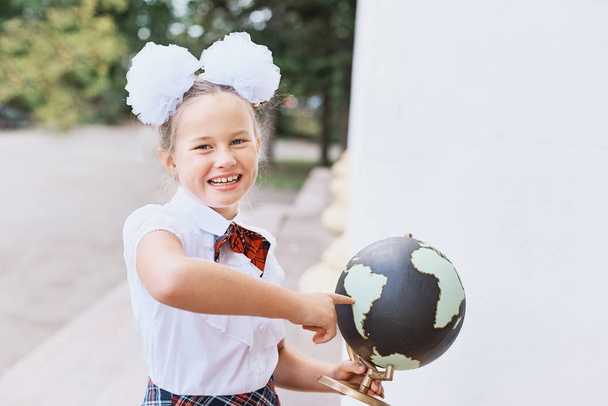 Portrait of beautiful young first-grader Farewell Bell. day of knowledge. beginning of the school year. school equipment. Young girl exploring the globe. - Zdjęcie, obraz