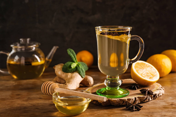 Чашка вкусного напитка с лимоном, имбирем и медом на деревянном столе
 - Фото, изображение