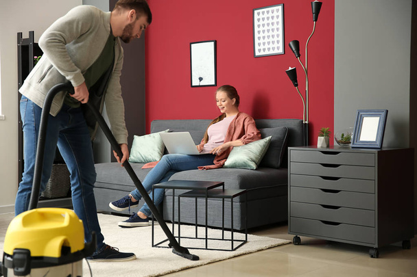 Hausmann putzt Fußboden, während seine Frau zu Hause arbeitet - Foto, Bild