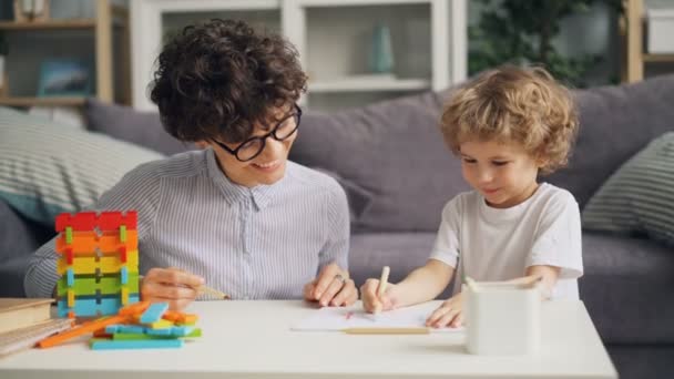 Little boy drawing picture with pencils while cheerful woman talking and smiling - Materiał filmowy, wideo