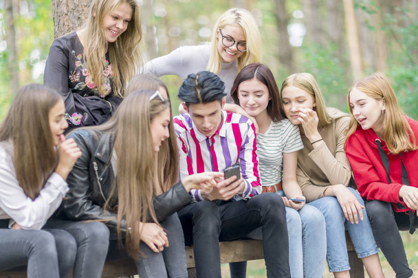 Young people sitting on a bench in the woods and look at the pho - Фото, зображення
