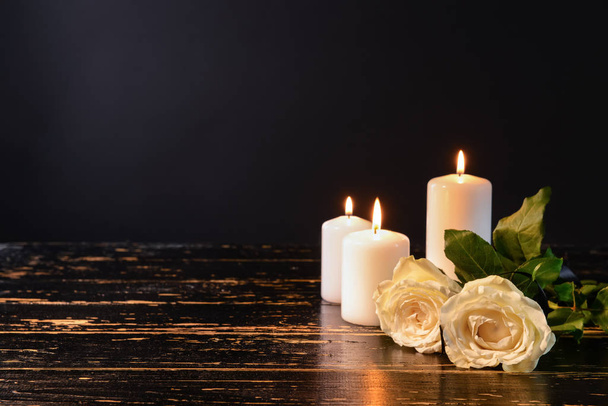 Burning candles and flowers on table against black background - Photo, Image