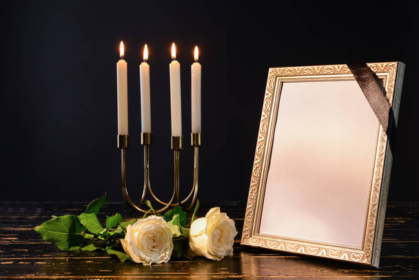 Порожня похоронна рамка, свічки та квіти на столі на чорному тлі
 - Фото, зображення
