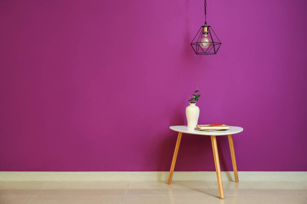 Стол с вазой и новой лампой висит на цветной стене
 - Фото, изображение