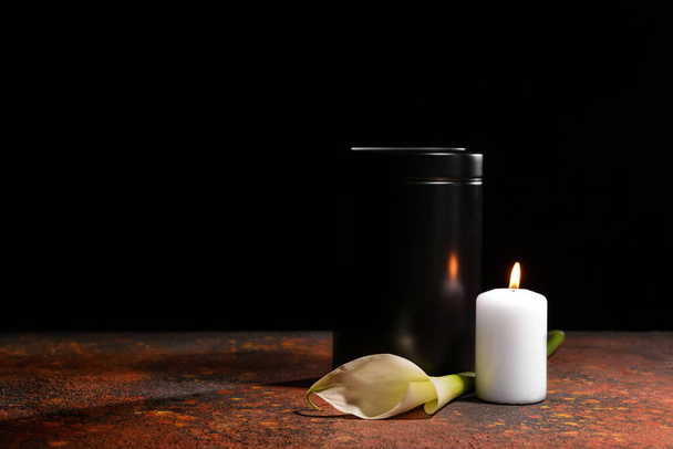Mortuary urn, burning candle and flower on table against dark background - Foto, afbeelding