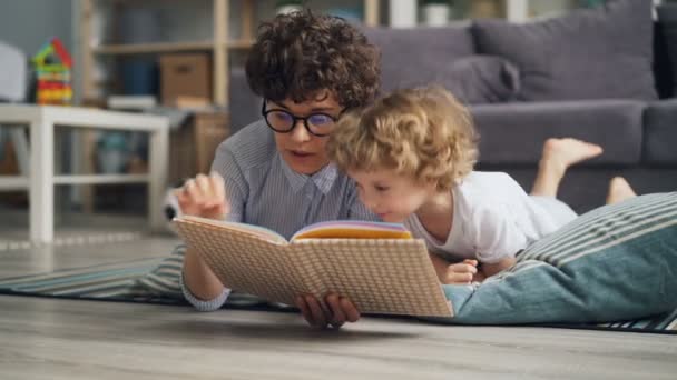 Happy family young woman and little boy reading book lying on blanket at home - Filmmaterial, Video