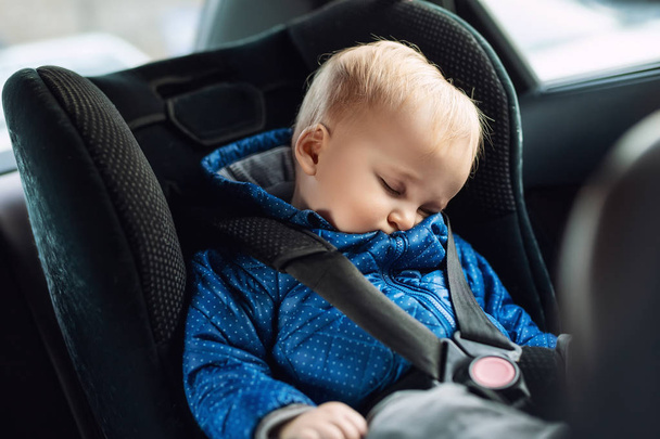 Cute caucasian toodler boy sleeping in child safety seat in car during road trip. Adorable baby dreaming asleep in comfortable place during journey in vehicle. Children care and safety on road - Фото, изображение