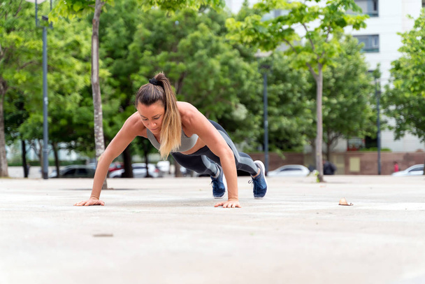 An athletic woman doing push ups in the park - Valokuva, kuva