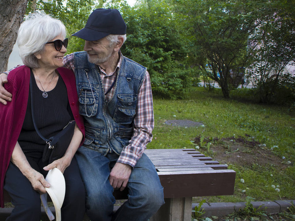 Heureux couple souriant âgé assis sur le banc dans le parc, l'homme regarde la femme avec amour
 - Photo, image