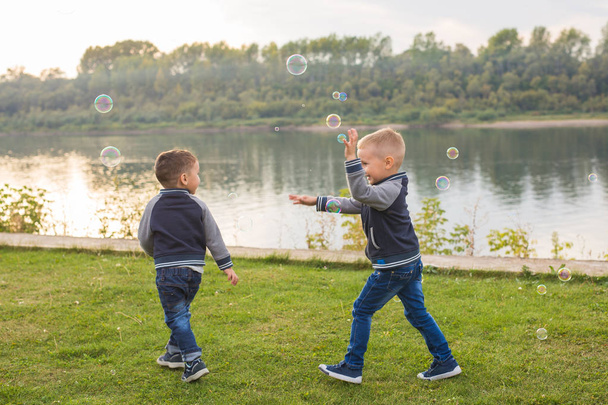 Children and nature concept - Little Brothers trying to catch soap bubbles - Photo, Image