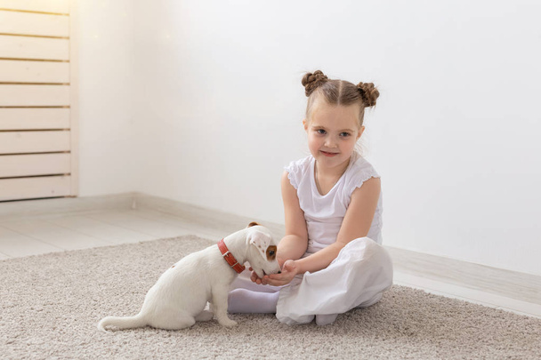Dzieci, zwierzęta domowe i zwierzęta koncepcja - dziecko dziewczynka w piżamie, grając z Jack Russell Terier szczeniak na podłodze - Zdjęcie, obraz