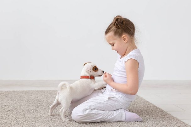 Emberek, a háziállat és az állatok koncepció - kis lány ül a földön fehér háttér és a gazdaság kiskutya Jack Russell Terrier - Fotó, kép
