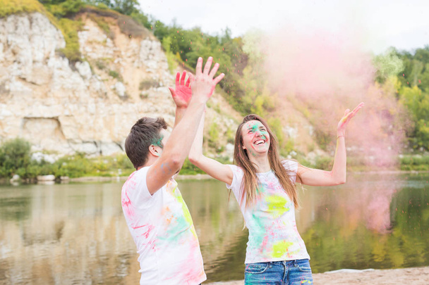 Festival holi, holidays, tourism and nature concept - Couple dressed in white shirts playing with colorful dust - Foto, imagen