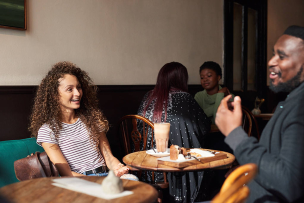 Dos jóvenes amigos riendo mientras beben café y hablan juntos en un café de moda
 - Foto, Imagen