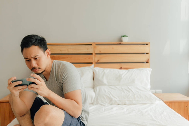 Man is playing mobile game with his smartphone on the bed. - Foto, imagen