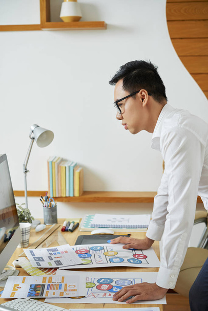 Professional graphic designer leaning to table to check colors of logotype on computer screen - 写真・画像