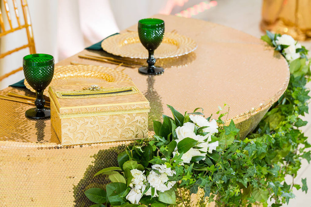Zlaté nádobí, zelené sklenice na víno a ubrousky. Stravovací koncept. Vnitřek stanu pro svatební hostiny, připraveno pro hosty. Sloužil kolo slavnostní stůl. - Fotografie, Obrázek