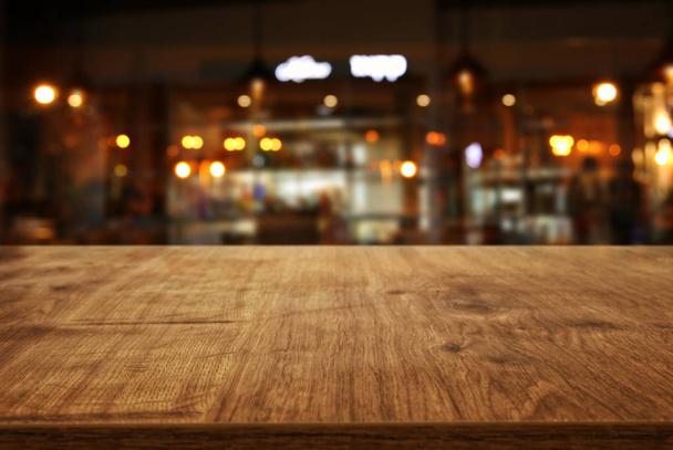 Image of wooden table in front of abstract blurred restaurant lights background - Foto, afbeelding