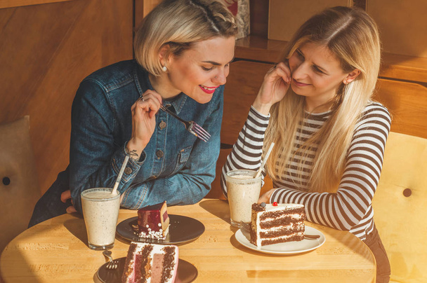 Twee gelukkige vrouwen zitten in een cafe, een cocktail drinken, vertellen elkaar grappige verhalen, in een goed humeur, gelukkig lachen - Foto, afbeelding