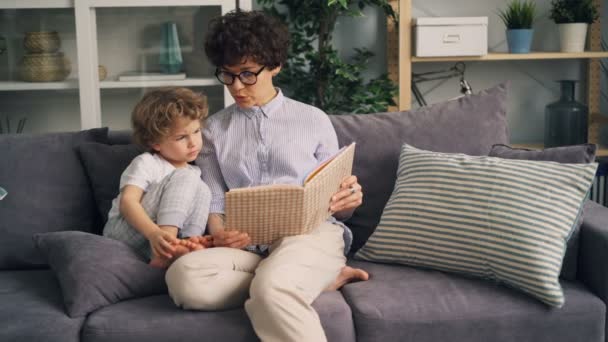 Cheerful woman reading funny story to little boy laughing having fun at home - Filmmaterial, Video