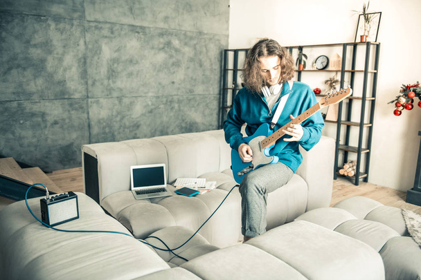 Artistic young man actively playing on guitar in the middle of the room - 写真・画像