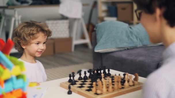 Mother teaching cute boy to play chess while child is having fun moving pieces - Πλάνα, βίντεο