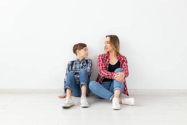 Family, mothers day and teenager concept - Portrait of mother and son sitting on the floor - Photo, Image