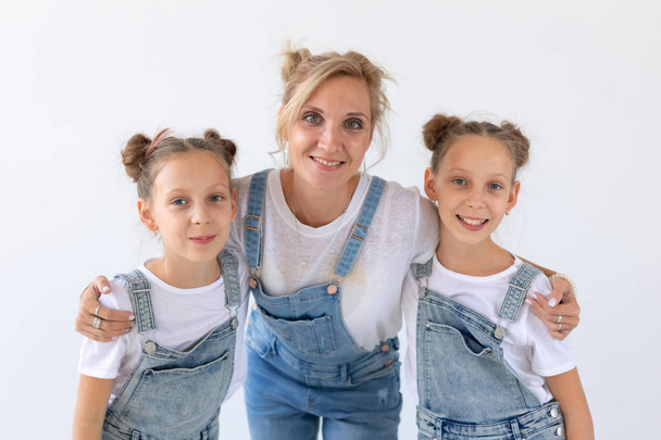 Perhe, siskot ja rakkaus konsepti - Äiti halaa kahta kaksoistytärtä valkoisella taustalla
 - Valokuva, kuva