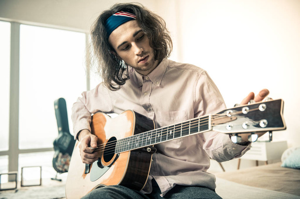 Attentive good-looking man with wavy hair tuning strings on acoustic guitar - Фото, зображення